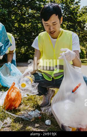 Giovane volontario maschile che raccoglie materie plastiche al parco Foto Stock