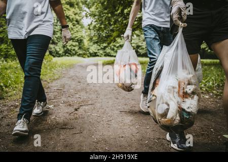 Sezione bassa di volontari maschi e femmine con sacche di plastica nel parco Foto Stock