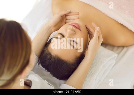 Primo piano della massaggiatrice professionale che fa il massaggio del viso e della testa per il suo cliente femminile. Foto Stock