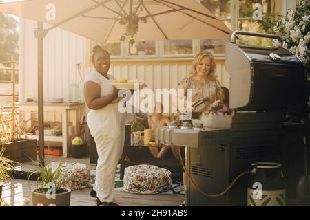 Donne sorridenti che preparano il cibo sulla griglia del barbecue nel patio Foto Stock