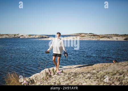 Uomo adulto medio in piedi su roccia contro il mare durante le vacanze estive Foto Stock