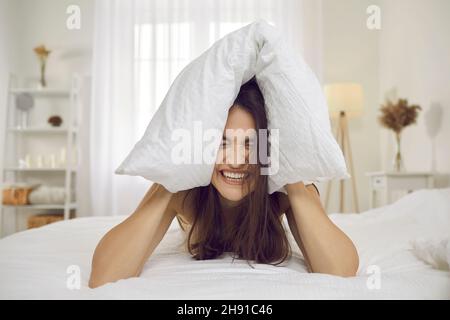 Capricciosa, pazza e aggressiva donna che grida forte e copre le sue orecchie con cuscino. Foto Stock