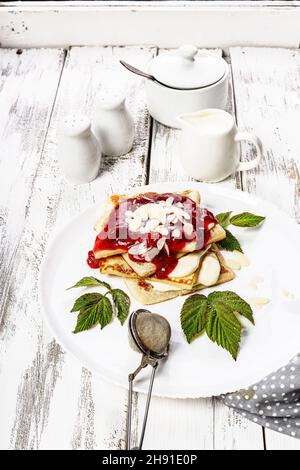 Frittelle tradizionali e deliziose con marmellata di fragole. Colazione gustosa. Pancake fatti in casa con marmellata su sfondo bianco rustico. Servizio di stoviglie bianche. Foto Stock
