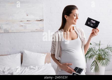donna sorridente e incinta in possesso di ecografie Foto Stock