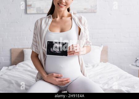 vista parziale di una donna incinta allegra che esegue la scansione a ultrasuoni Foto Stock
