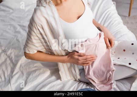 vista parziale della donna incinta tatuata che tiene i rimpelli del bambino nella camera da letto Foto Stock