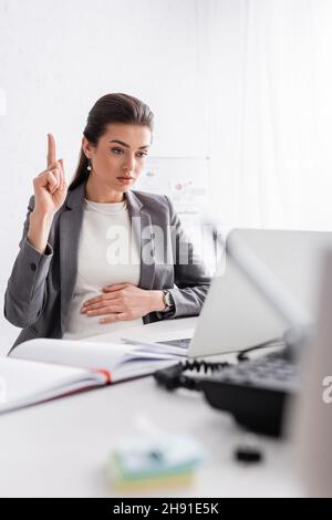 giovane donna d'affari incinta che punta in su e guarda il laptop in ufficio Foto Stock