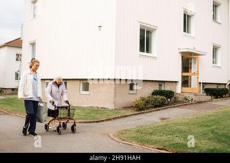 Caregiver domestico femminile che cammina con la donna anziana costruendo sul sentiero Foto Stock