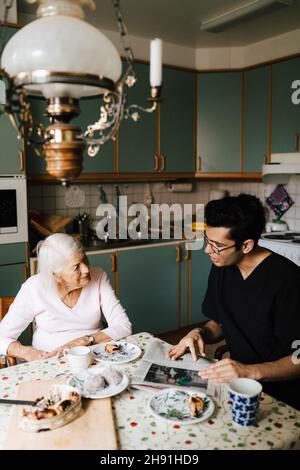 Salute maschile parlare con la donna anziana mentre si legge il giornale al tavolo da pranzo Foto Stock