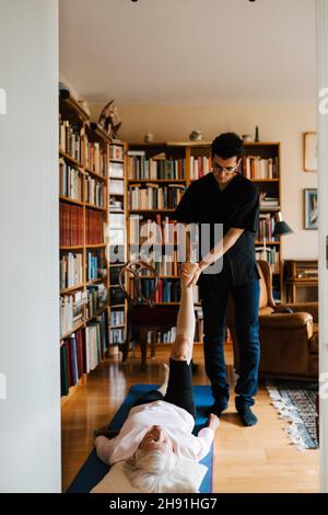 Giovane operatore sanitario maschile che guida la donna anziana mentre si esercita in soggiorno Foto Stock
