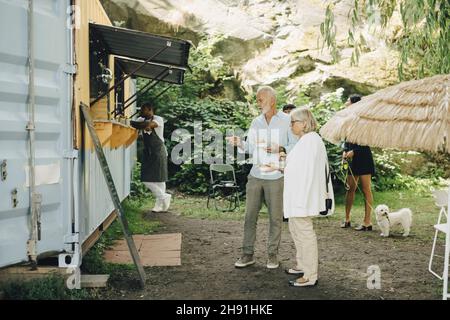 Uomo e donna anziana che parlano mentre mangiano fuori dal camion nel parco Foto Stock