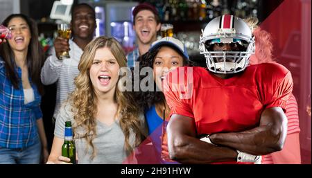 Immagine composita digitale del giocatore di calcio americano con le braccia incrociate contro i tifosi eccitati Foto Stock