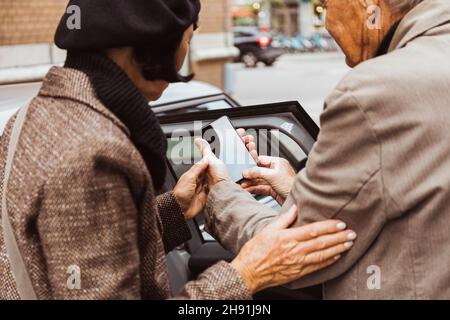 Coppia anziana che utilizza lo smartphone in piedi fuori dall'auto in città durante il weekend Foto Stock