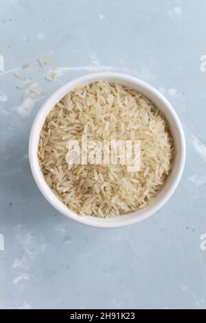 Riso bianco macinato a grani lunghi in una ciotola bianca su sfondo grigio. Concetto di cibo vegetariano. Orientamento verticale. I piatti di riso sono cucinati in tutto il conto Foto Stock