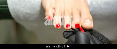 Pedicurista che applica smalto rosso alle unghie femminili in un salone di bellezza Foto Stock