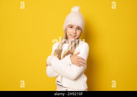 Giovane donna sorridente in abbigliamento invernale che si abbraccia in piedi isolato su sfondo giallo. Foto Stock