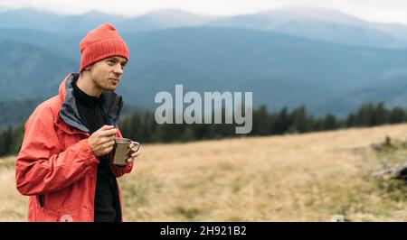 Ritratto di uomo turistico caucasico mangiare fast food in montagna, spaghetti istantanei per il viaggiatore, delizioso pranzo in natura mentre rilassante. Foto Stock