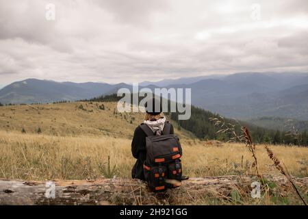 Vista posteriore del concetto di stile di vita e sopravvivenza. La donna escursionistica con uno zaino è molto stanca e si siede su una sosta godendo l'escursione in background nel Foto Stock