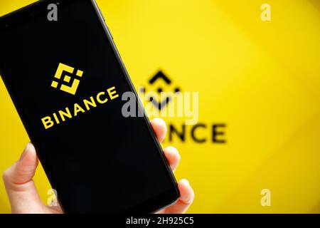 Ucraina, Odessa - 9 ottobre 2021: Tenere a mano il cellulare con l'app Binance in esecuzione sullo schermo dello smartphone con il logo Binance sullo sfondo. Binance è una piattaforma di scambio e scambio di criptovaluta Foto Stock