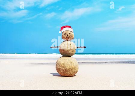 Natale positivo pupazzo di neve di sabbia in rosso di Santa Claus hat a ocean Sunset beach. Nuovo anno Sconti vacanze in paesi caldi concetto destinazioni Foto Stock