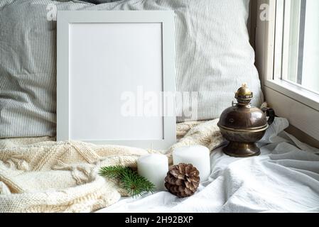 Accogliente inverno casa interior scene.Christmas composizione vicino alla window.blank bianco pictur cornice mockup, lampada a olio, candele, pino cono.modello per Natale Foto Stock