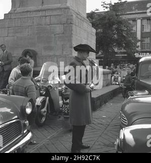 1965, storica, Ripon piazza della città, un hornblower guardato dai visitatori della città, casa di un antico Cathedal, Ripon, Yorkshire, Inghilterra, Regno Unito. Risalente al 886, un Wakeman ha tenuto sotto controllo la città di Ripon, assicurando che ci fosse qualcuno in guardia di notte. Ogni sera alle 9:00 per centinaia di anni, il soffiatore ha suonato il suo corno quattro volte intorno alla croce del mercato presso la piazza del mercato Ripon. Foto Stock