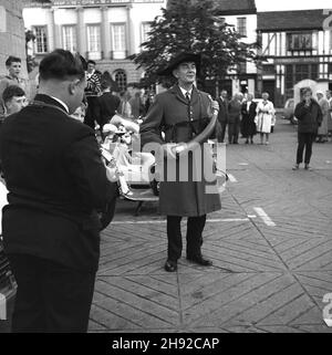 1965, storica, Ripon piazza della città, un hornblower guardato dai visitatori della città, casa di un antico Cathedal, Ripon, Yorkshire, Inghilterra, Regno Unito. Risalente al 886, un Wakeman ha tenuto sotto controllo la città di Ripon, assicurando che ci fosse qualcuno in guardia di notte. Ogni sera alle 9:00 per centinaia di anni, il soffiatore ha suonato il suo corno quattro volte intorno alla croce del mercato presso la piazza del mercato Ripon. Foto Stock