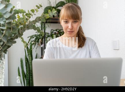 Donna che lavora su un computer portatile circondato da piante e fiori sul balcone durante il giorno Foto Stock