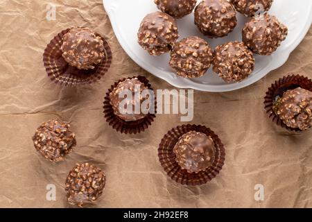 Diversi cioccolatini dolci con noci e piatti bianchi su carta artigianale, primo piano, vista dall'alto. Foto Stock