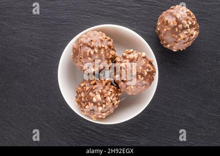 Quattro cioccolatini dolci con noci e un piattino in ceramica su una pietra ardesia, da vicino, vista dall'alto. Foto Stock