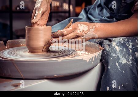 Primo piano UN vasaio donna in splendidamente scolpisce una ciotola profonda di creta marrone e taglia fuori creta eccedente su un ruota di potter in una bella officina Foto Stock