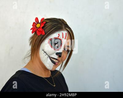 Giovane donna messicana attraente dipinge la metà destra del suo volto con spaventoso bianco Catrina viso make-up il giorno dei morti e guarda lo spettatore. Foto Stock