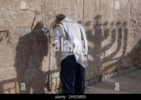 Un ebreo religioso avvolto con Talit Shawl prega come la Menorah, uno dei simboli del giudaismo, poiché i tempi antichi gettano ombra sul muro occidentale o Kotel durante la festa ebraica di Hanukkah, il festival delle luci nella città vecchia Gerusalemme est Israele Foto Stock