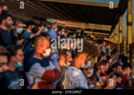 Non focalizzato sfocato volto mascherato spettatori guardando la partita in piedi nello stadio con un telefono cellulare nelle loro mani. Foto Stock