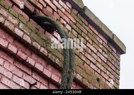 Un vecchio cavo elettrico sporco nel muro di mattoni della facciata di una casa abbandonata. Foto Stock