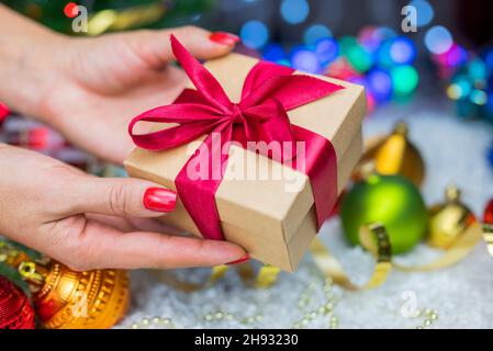 Confezione regalo con un arco nelle mani di una ragazza con una serpentina e giocattoli di Natale sullo sfondo di un albero di Natale e bokeh per il nuovo anno Foto Stock