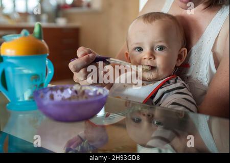 Una bambina (ca. 10 mesi) è stato cucchiaio alimentato la sua colazione in grembo di sua madre. Foto Stock