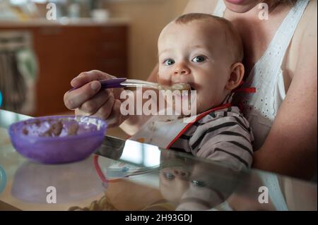 Una bambina (ca. 10 mesi) è stato cucchiaio alimentato la sua colazione in grembo di sua madre. Foto Stock