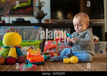 Una bambina (ca. 10 mesi) studia un giocattolo mentre gioca a casa. Foto Stock