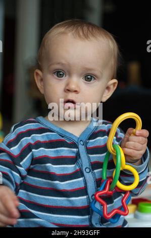 Una bambina (ca. 10 mesi) gioca con un giocattolo di plastica colorato a casa. Foto Stock