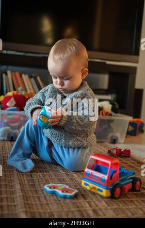 Una bambina (ca. 10 mesi) studia un giocattolo mentre gioca a casa. Foto Stock