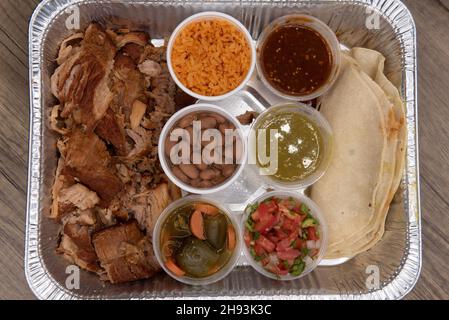 Vista dall'alto di porzioni a grandezza familiare di carne di maiale carnitas con riso, fagioli e salsa per avere tacos per tutti. Foto Stock