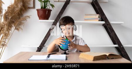 lezione di geografia uno scolaro con un globo ascolta una lezione di audio online tramite cuffie o cuffie wireless. Formazione a distanza e compiti Foto Stock