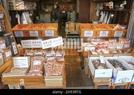 Un vecchio negozio nel quartiere Tsukiji di Tokyo con interni in legno che vendono prodotti di pesce secchi assortiti. Il fornitore è all'interno del negozio. Foto Stock