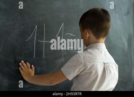 il ragazzo della classe vicino alla lavagna scrive i numeri con il gesso. Lezione di matematica. Scuola Junior. Concetto di educazione moderna. Torna a scuola. Luogo Foto Stock