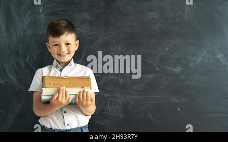 Felice studente universitario in piedi accanto al bordo del gesso in classe con libri di testo o libri in mano. Ridendo studente di scuola elementare. Anno accademico Foto Stock