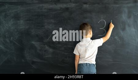 L'allievo in classe in una lezione di matematica scrive su una tavola di gesso con gesso. Lezione di matematica della scuola elementare. Concetto di apprendimento. Torna a scuola. Banner e luogo Foto Stock