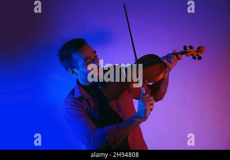 Uomo che suona il violino su luci al neon a bassa luminosità da studio Foto Stock