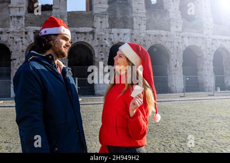 Tempo di shopping di Natale. Coppia giovane con cappello Babbo Natale che posa di fronte al Colosseo. Mostra la sua carta di credito per andare a fare shopping, ma non è più Foto Stock