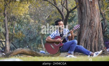 giovane ragazzo con la chitarra e suonare la chitarra nel parco Foto Stock